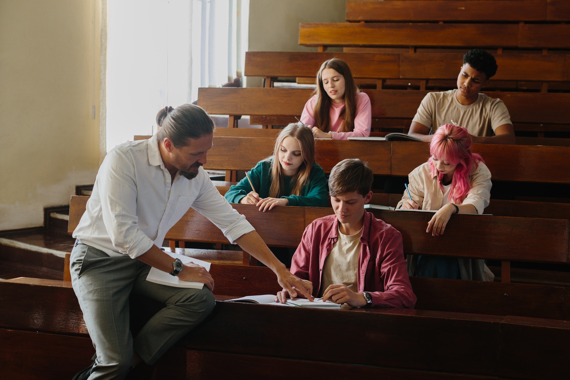 Teacher Assisting Students in University Lecture Hall for Engaged Learning